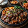 A sizzling plate of vegan bulgogi made with plant-based protein, glazed with a rich Korean BBQ sauce, and garnished with sesame seeds and green onions. Served with traditional Korean side dishes like kimchi, pickled radish, and steamed rice on a wooden table