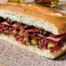 A close-up of a classic New Orleans Muffuletta sandwich with layers of Italian meats, provolone cheese, and a tangy olive salad, served on a crusty sesame loaf.